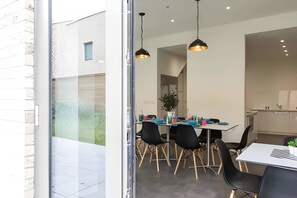 A modern dining area with a glass partition, black chairs, a white table, and pendant lighting. - Student Only The Cam Foundry (Cambridge)