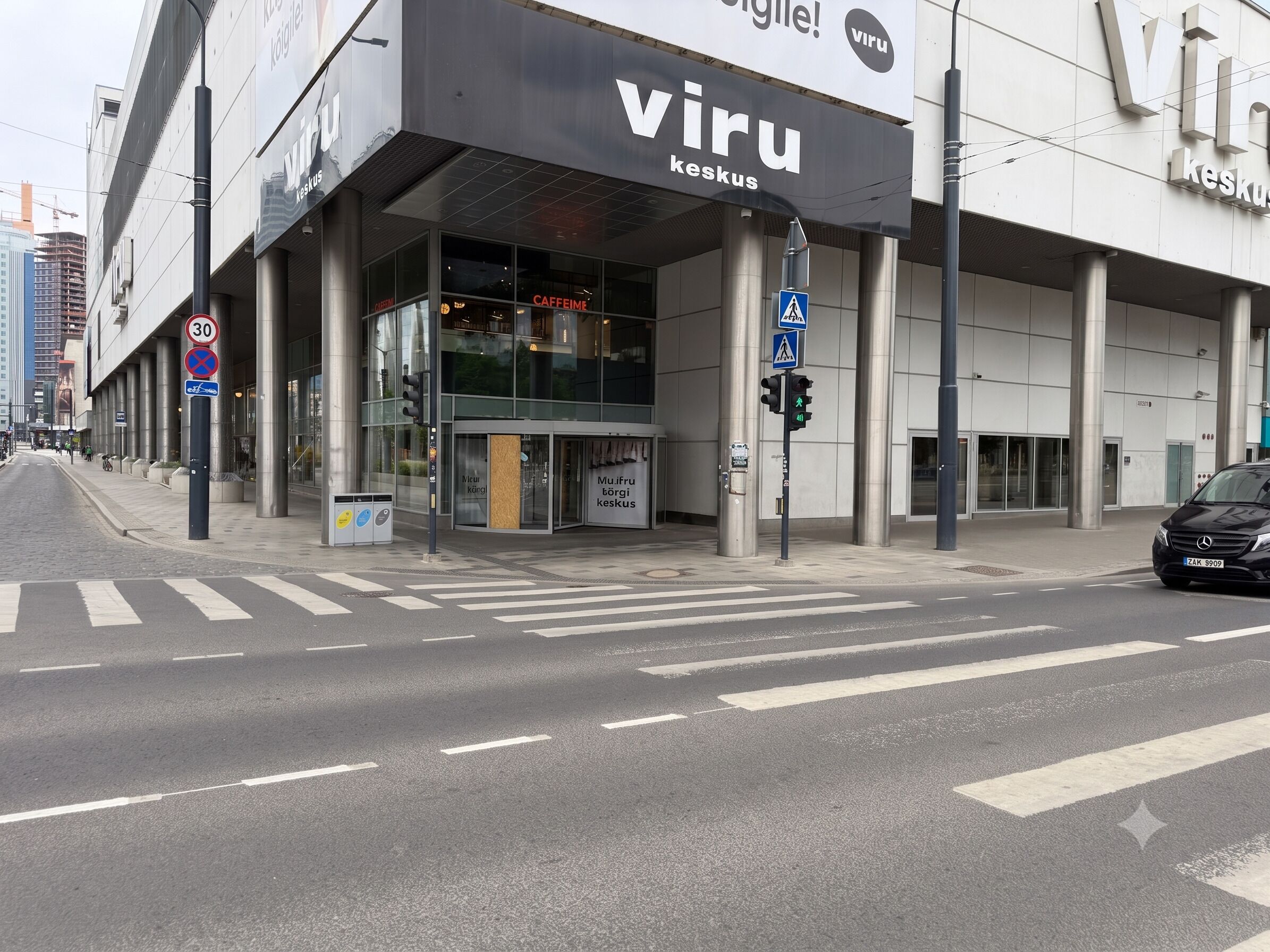 Ein modernes Gebäude mit einer großen Schrifttafel, auf der 'viru keskus' steht, und einem Fußgänger überweg.