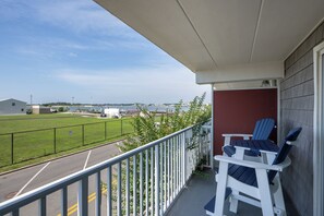 Ein Balkon mit zwei Adirondack-Stühlen, Blick auf ein Sportfeld und ein Gebäude im Hintergrund.