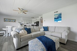 Ein Wohnzimmer mit einem Ecksofa, einem Esstisch und einer Küche im Hintergrund.