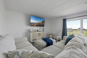 Ein modernes Wohnzimmer mit großem Flachbildfernseher, einer Sofagarnitur, einem Beistelltisch und Blick ins Freie.