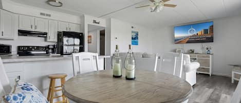 A modern kitchen with white cabinetry, a built-in oven, and a refrigerator. There is a dining area with a round table and chairs.