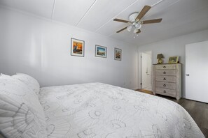 Ein Schlafzimmer mit einem Bett, einem Deckenventilator, einer Kommode und gerahmten Bildern an der Wand.