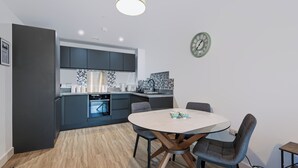 A modern kitchen with dark cabinets, a round dining table, and a clock on the wall. - Cozy Liverpool City Center 2BDR Stay (Liverpool)