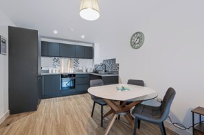 Eine moderne Küche mit dunklen Schränken, einem runden Esstisch und einer Uhr an der Wand.