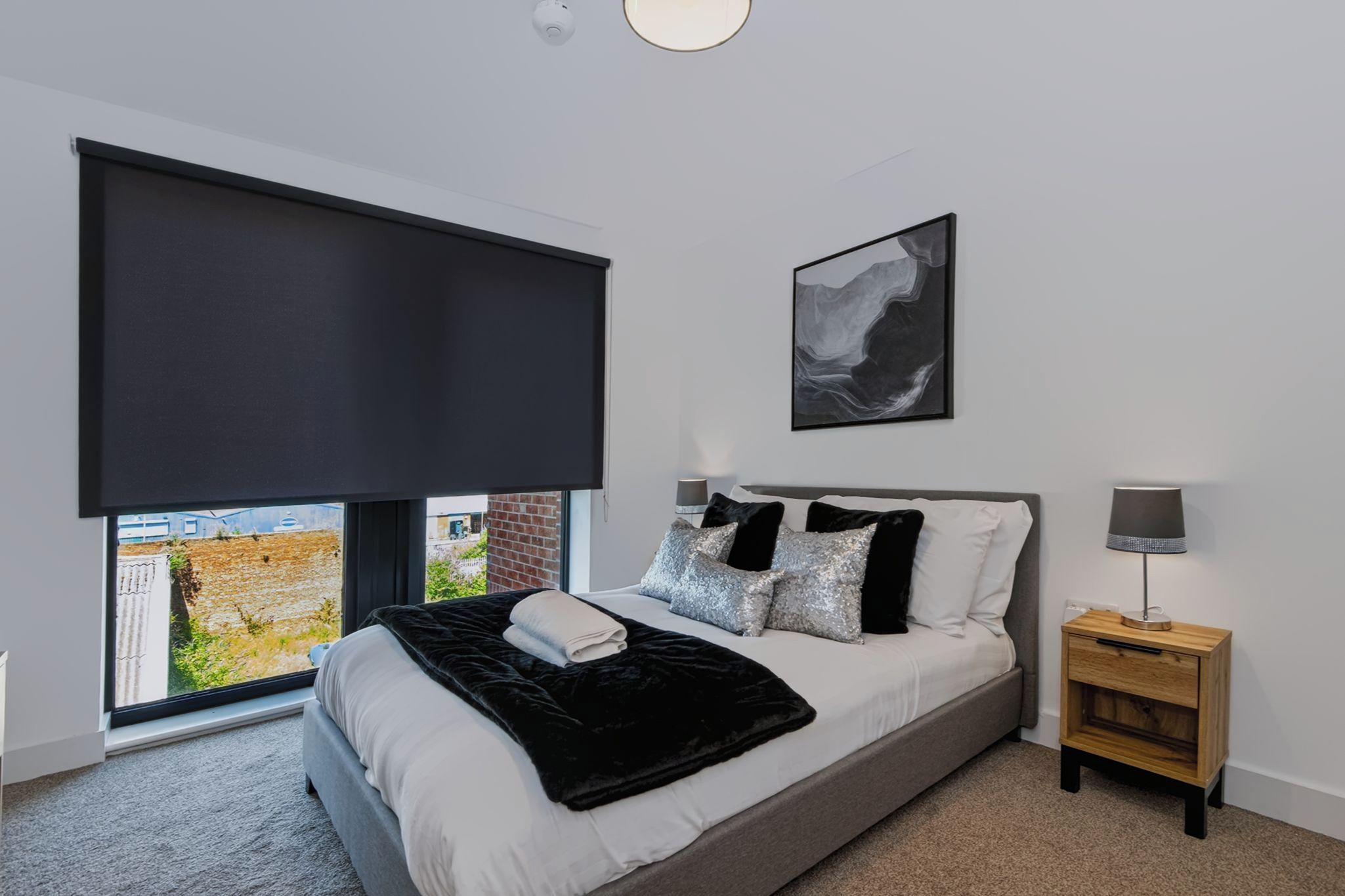 Une chambre à coucher avec un grand lit, une fenêtre donnant sur un beau paysage, une table de chevet et une œuvre d’art accrochée au mur.