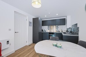 A modern kitchen with dark cabinets, a white countertop, and a marble dining table. - Cozy Liverpool City Center 2BDR Stay (Liverpool)