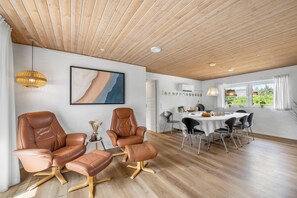 A spacious room with a wooden ceiling, a dining area with a round table and chairs, leather armchairs, and a large abstract painting on the wall. - Large pool house with spa, sauna and lovely outdoor areas (Ulfborg)