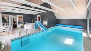 En indendørs swimmingpool med vandrutsjebaner, et boblebad og et opholdsområde.