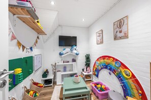 Ein Kinderzimmer mit weißer Wand, einem Fernseher und einer bunten Spielanlage.
