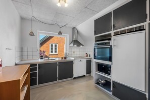 A modern kitchen with white and black cabinetry, a visible window, and a brick wall outside. - Charming holiday apartment on the 1st floor in Stadil (Tim)