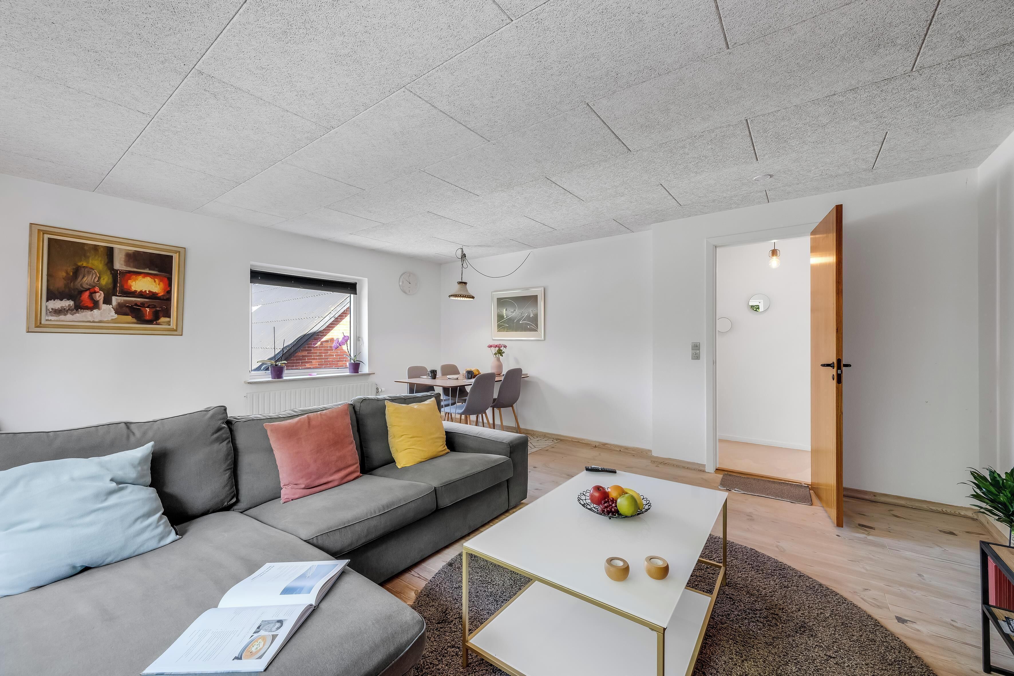 Un salon moderne avec un canapé gris, une table basse blanche et un coin repas à l’arrière-plan.