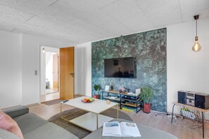 Una sala de estar moderna con un televisor de pantalla plana montado en una pared con textura, una mesa de centro, sofás y una estantería.