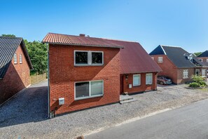 Ein zweistöckiges Backsteinhaus mit rotem Dach, einer Schotterauffahrt und einem geparkten Auto.