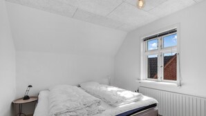 Ein Schlafzimmer mit einem Bett, einem Nachttisch, einer Lampe und einem Fenster mit Blick auf eine Backsteinmauer.
