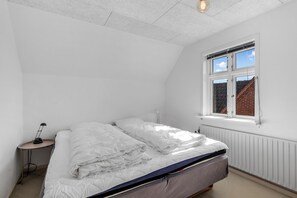 Ein Schlafzimmer mit einem Bett, einem Nachttisch, einer Lampe und einem Fenster mit Blick auf eine Backsteinmauer.