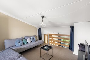 Ein modernes Zimmer mit einer Couch, einem kleinen Tisch, einem Fernseher und einem Balkon mit Holzgeländern.