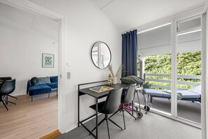 Ein modernes Zimmer mit Schreibtisch, Stühlen, einem Spiegel und Blick auf einen Balkon mit einem Bett.