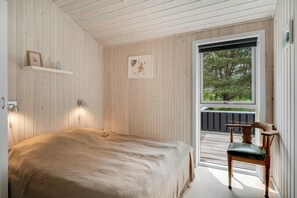 Ein Schlafzimmer mit Bett, Sessel, Fenster und Tür.