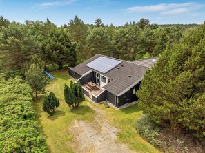 Een huis met een schuin dak, zonnepanelen, een terras en een schommel in een bebost gebied.