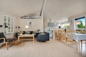 A spacious living area with a sofa, coffee table, and dining table set for six. - Modern holiday home with large enclosed terrace in quiet surroundings (Fjerritslev)