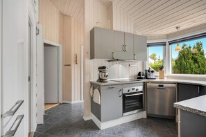 A modern kitchen with grey cabinets, a built-in oven, a dishwasher, and a window with a view of greenery. - Modern holiday home with large enclosed terrace in quiet surroundings (Fjerritslev)