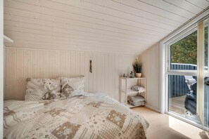 Een slaapkamer met een groot bed, een witte plank met decoratieve objecten en uitzicht door een groot raam.