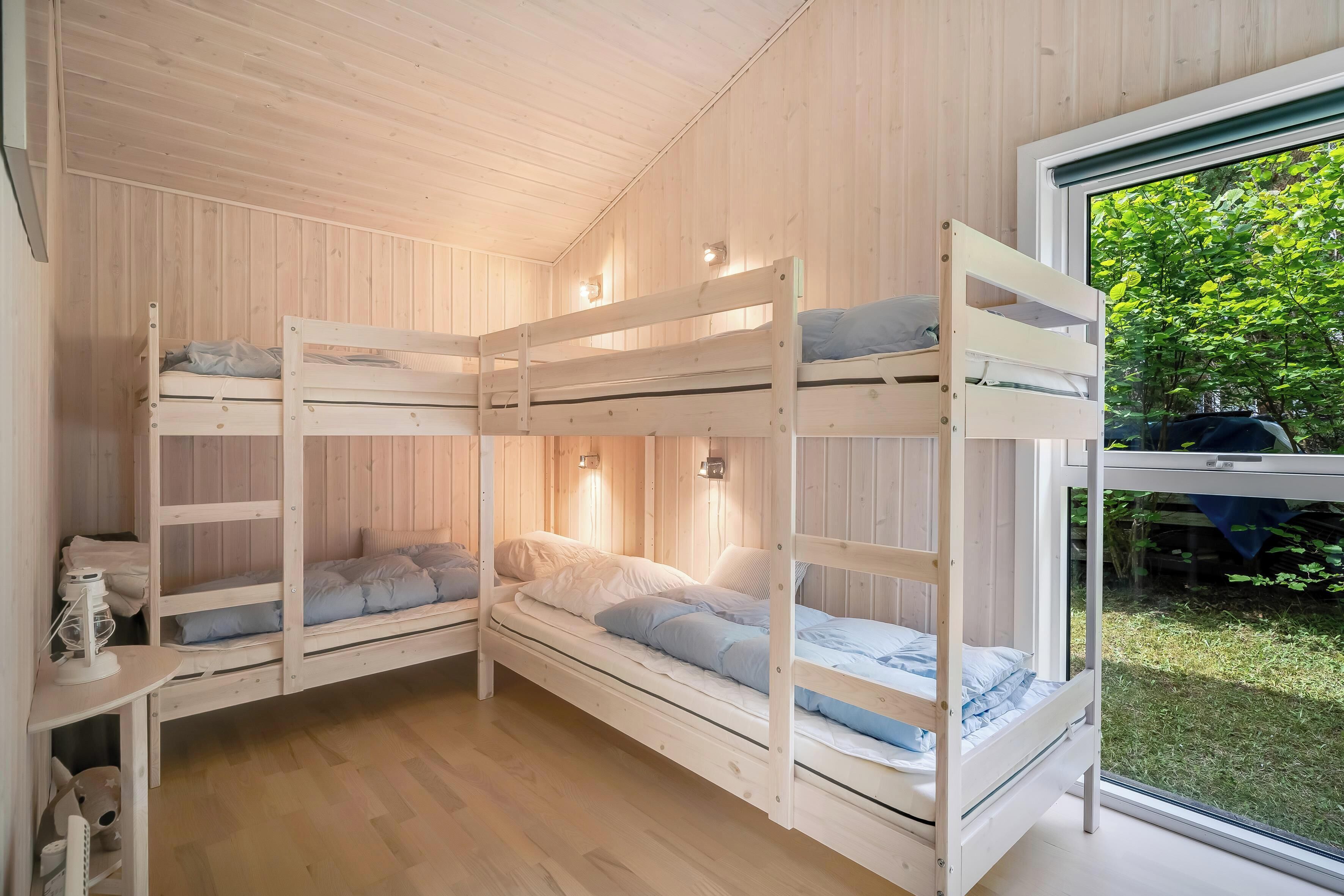 Quarto com beliches, paredes de madeira e janela com vista para um jardim.
