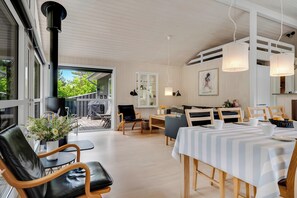A modern interior with a dining area, a seating arrangement, and a view through a glass door to an outdoor deck. - Modern holiday home with large enclosed terrace in quiet surroundings (Fjerritslev)