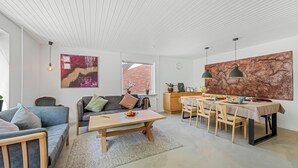En moderne stue med sofa, sofabord, spisebord og stole. Der er et vindue med udsigt til en murstensbygning.