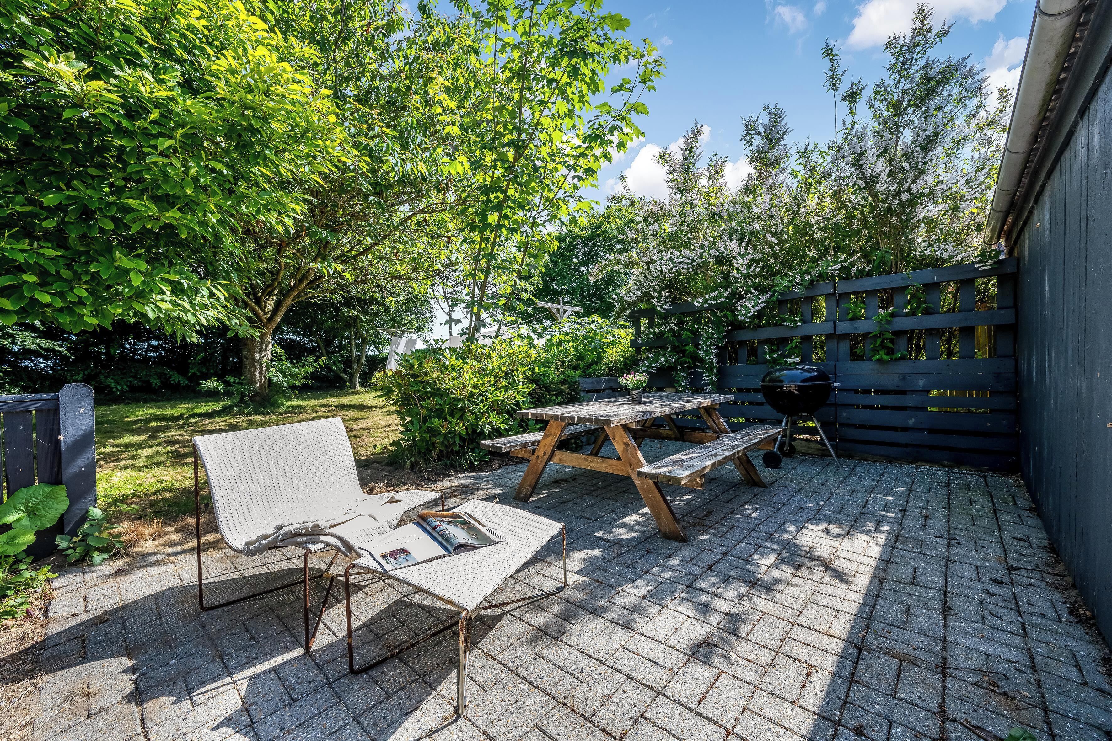 Un patio con una mesa y banco de madera, rodeado de árboles y una valla de madera.