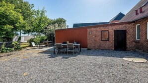 En terrasse med grus, et bord og stole, en murstensbygning med en dør og et træ i baggrunden.