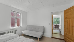 Et soveværelse med en seng, en grå sofa, et vindue og en trædør.