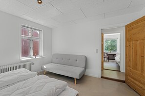 A bedroom with a bed, a grey sofa, a window, and a wooden door. - Modernized ground floor holiday apartment in Stadil (Tim)