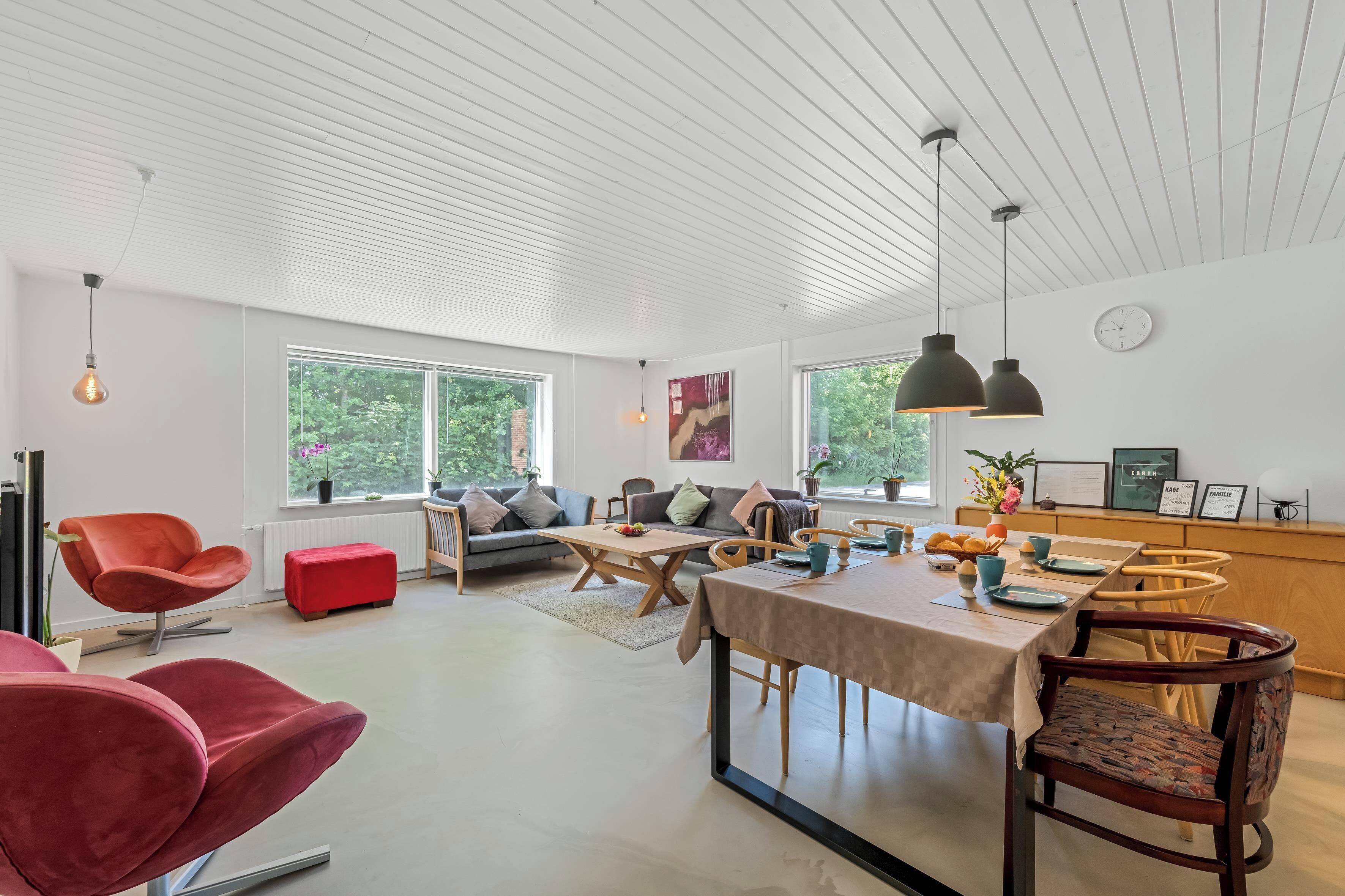 A modern living room with a sofa, red chairs, a dining table set, and pendant lighting.