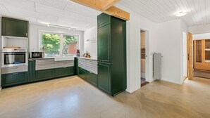 Et moderne køkken med indbyggede hårde hvidevarer, et stort vindue og udsigt til grøn natur.