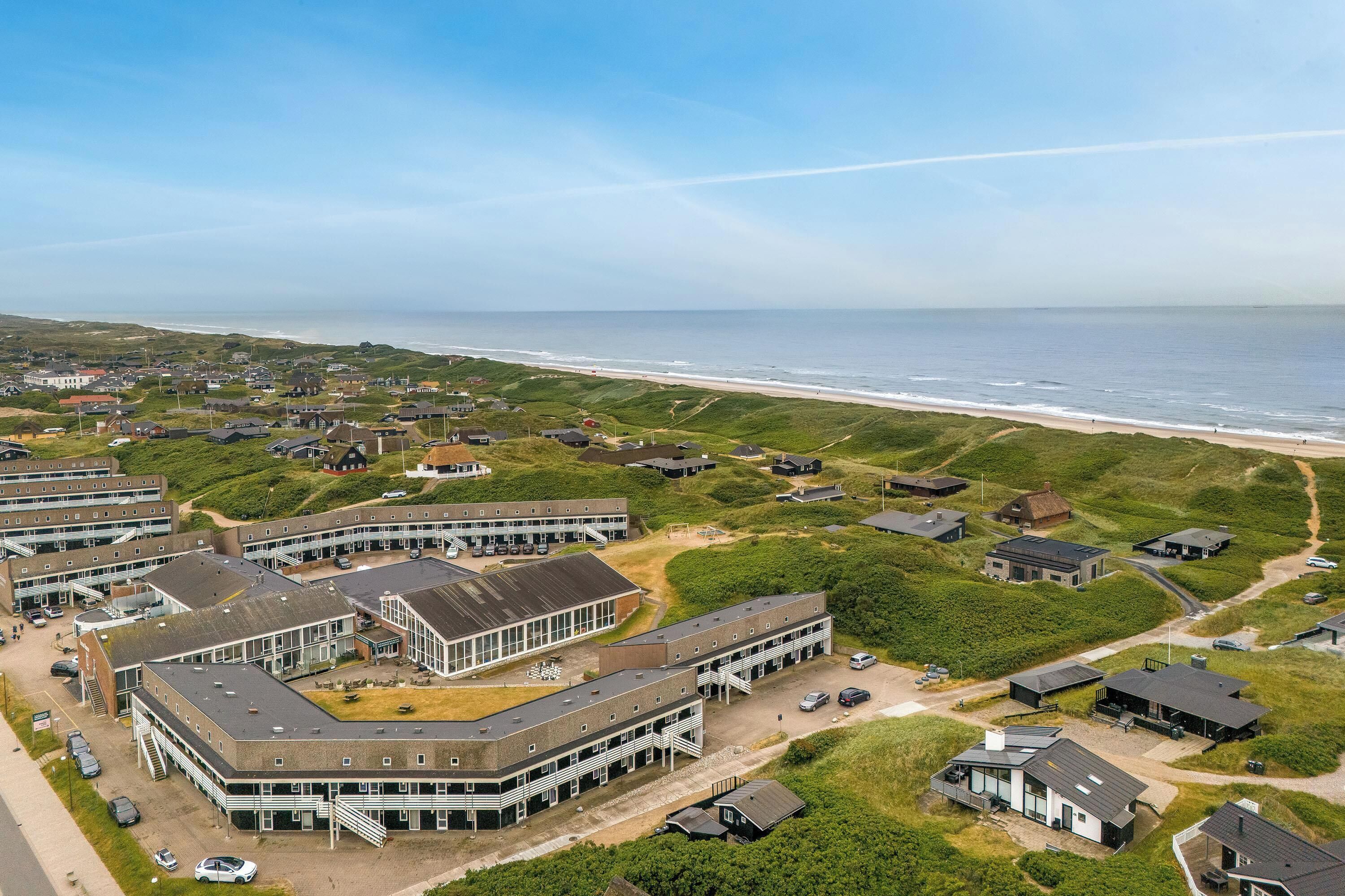 Eine Vogelperspektive auf ein Küstenwohngebiet mit Häusern, einem Strand und einem großen Gebäudekomplex mit mehreren Parkplätzen.