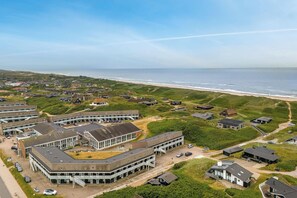 An aerial view of a coastal residential area with houses, a beach, and a large building complex with multiple parking areas. - Bright and newly renovated holiday apartment close to the North Sea and. (Ringkøbing)