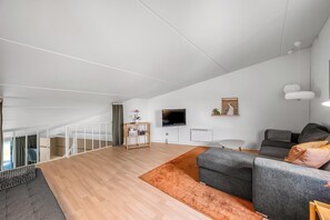 Een ruime woonkamer met een trap, een flatscreen-tv, een grijze bank en een houten bijzettafeltje.