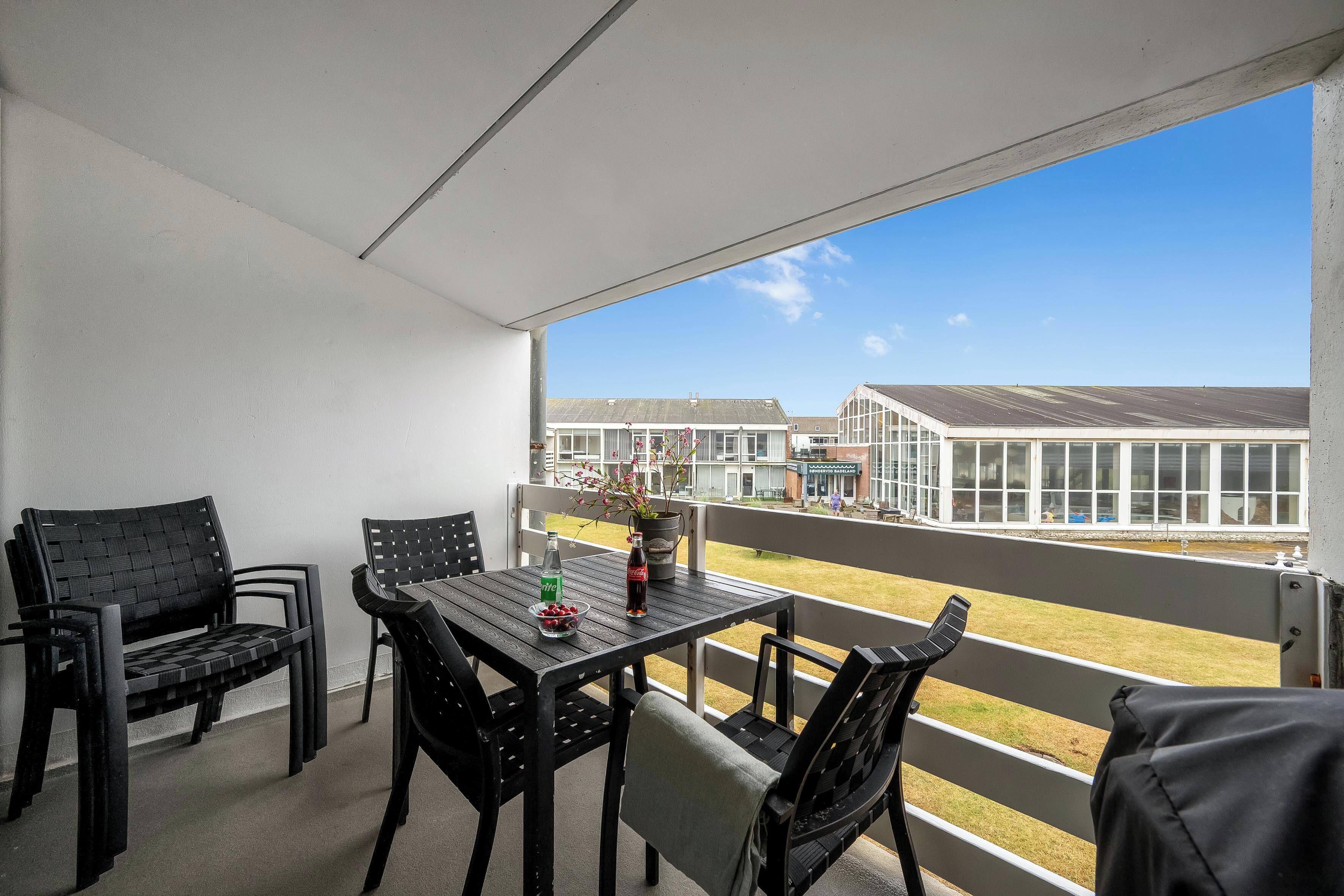 Un balcon avec une table et des chaises, une bouteille de Coca-Cola et un saladier rempli de fruits.
