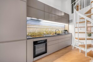 A modern kitchen with a built-in oven, a sink, and a staircase leading to an upper level. - Bright and newly renovated holiday apartment close to the North Sea and. (Ringkøbing)