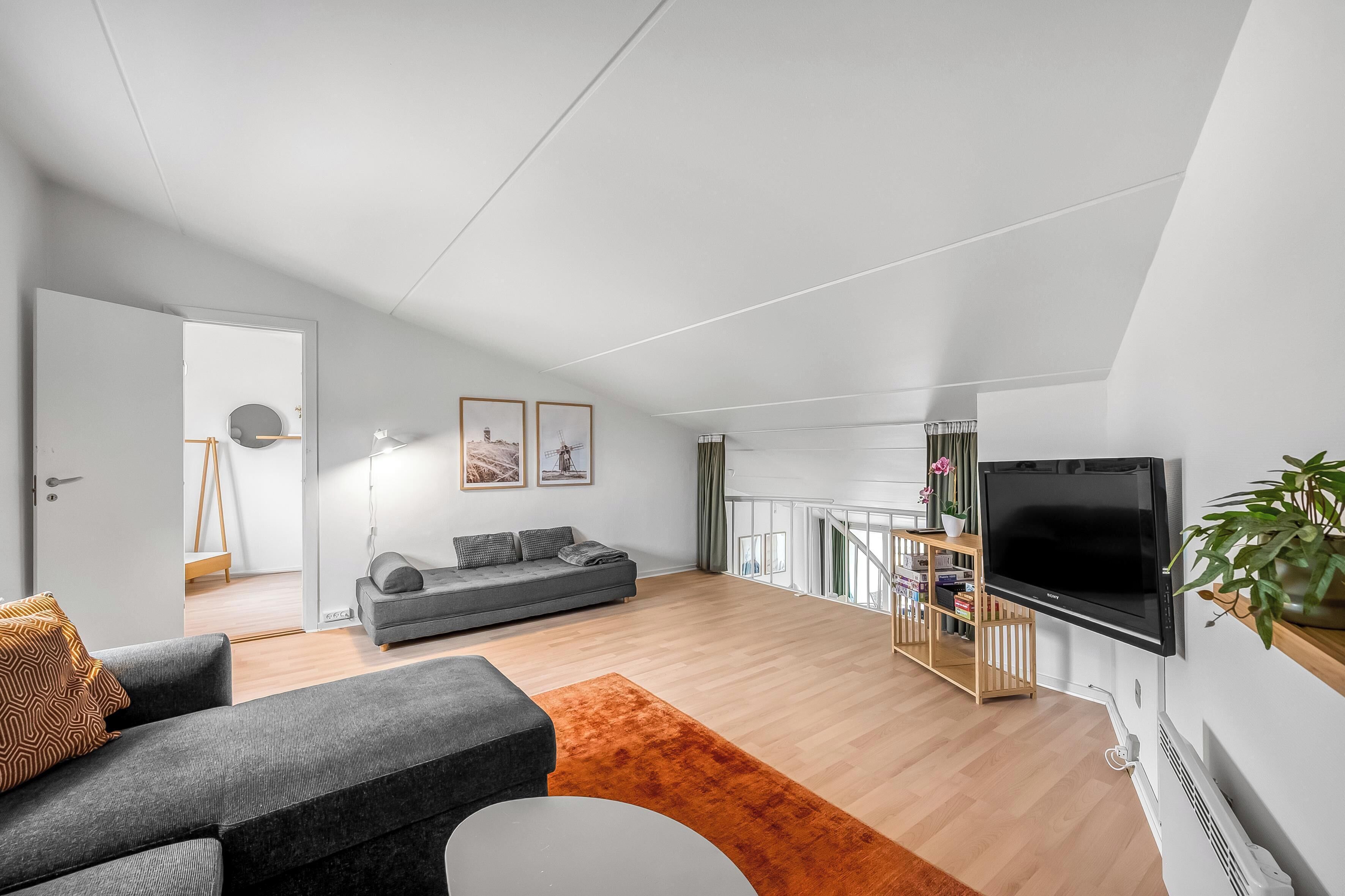 A modern living room with a grey sofa, a white coffee table, and a large flat-screen TV mounted on the wall. - Bright and newly renovated holiday apartment close to the North Sea and. (Ringkøbing)