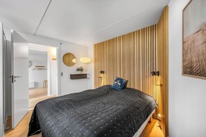 A bedroom with a bed, a wooden slat wall, a mirror, a wall-mounted light, and a hanging plant. - Bright and newly renovated holiday apartment close to the North Sea and. (Ringkøbing)