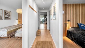 A narrow hallway with a bed on the left, a wooden wall on the right, and a door leading to a room with a bed. - Bright and newly renovated holiday apartment close to the North Sea and. (Ringkøbing)