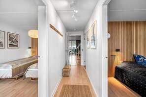 A narrow hallway with a bed on the left, a wooden wall on the right, and a door leading to a room with a bed. - Bright and newly renovated holiday apartment close to the North Sea and. (Ringkøbing)