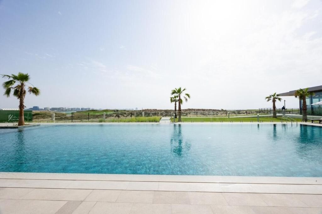A swimming pool with clear blue water, surrounded by a tiled deck and palm trees.