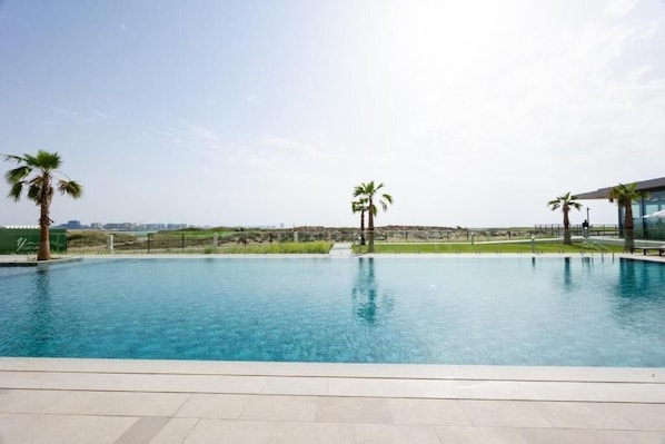 A swimming pool with clear blue water, surrounded by a tiled deck and palm trees. - Bloomfields 2Br in Fairways 3 (Abu Dhabi)