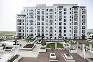 A multi-story residential building with balconies, a landscaped courtyard, and a view of the sea. - Bloomfields 2Br in Fairways 3 (Abu Dhabi)