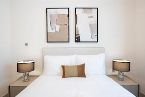 A hotel room with a bed, two nightstands, two lamps, and two abstract paintings on the wall. - Bloomfields 2Br in Fairways 3 (Abu Dhabi)