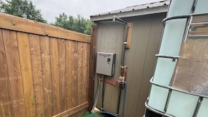 A backyard with a wooden fence, a water heater, and a glass enclosure. - Romantic Cabin Escape in Dawn Euphemia Sunsets & S'mores (Dawn-Euphemia)